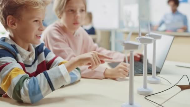 Schulmädchen und Schuljunge arbeiten mit dem Prototyp einer Windkraftanlage und lernen etwas über Umwelt und erneuerbare Energien. Naturwissenschaftlicher Grundschulunterricht mit Kindern, die an der Technik arbeiten. MINT-Ausbildung — Stockvideo