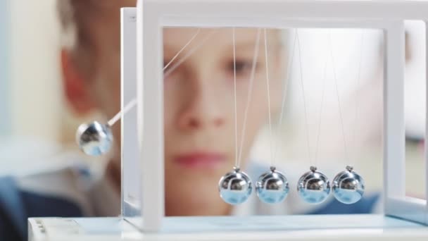 Close-up Retrato de um menino jovem curioso Olhando para berço de Newton. Aprendizagem de crianças sobre física — Vídeo de Stock