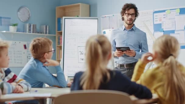 Profesor de Física de la Escuela Primaria utiliza la tableta digital interactiva para mostrar a un aula de niños inteligentes cómo funcionan las energías renovables y las turbinas eólicas. Clase de ciencias con niños escuchando atentamente — Vídeo de stock