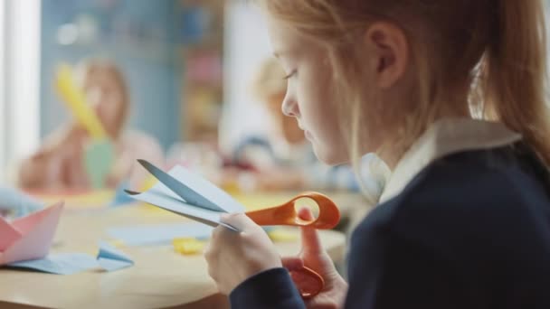 Bastelkurs der Grundschule: Über die Schulter eines Mädchens hat Spaß beim Bastelprojekt, bei dem Papierfiguren mit der Schere geschnitten werden. Kreative junge Mädchen — Stockvideo