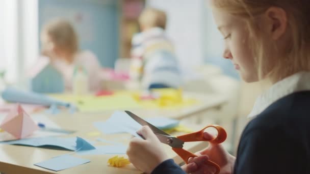 Δημοτικό Σχολείο Τεχνών & Χειροτεχνίας Τάξη: Πάνω από τον ώμο ενός κοριτσιού έχει διασκέδαση για το έργο Χειροτεχνίας, κόβει τις μορφές χαρτί με ψαλίδι. Δημιουργικό νεαρό κορίτσι — Αρχείο Βίντεο