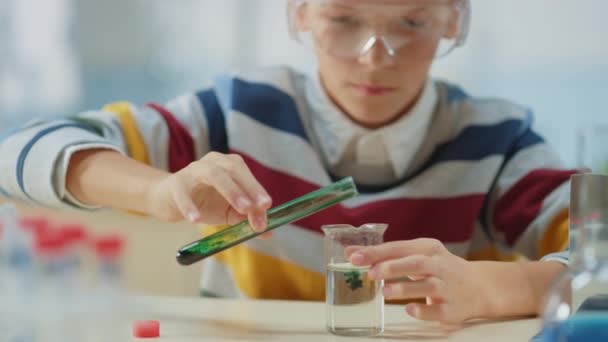 Elementary School Science Classroom: Smart Little Boy, одягнений в Safety Glasses, змішує хімічні речовини в Beakers — стокове відео