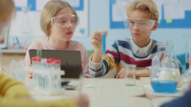 Escola Primária de Ciência Sala de aula: Smart Boy Mistura Produtos Químicos em Beakers e Garota Bonita Escreve e Analisa Resultados com Tablet Digital Computer. Educação Moderna, Aprendizagem Química — Vídeo de Stock