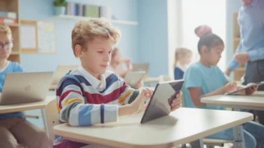 İlköğretim Okulu Bilgisayar Bilimi Sınıfı: Şirin Çocuk Dijital Tablet Bilgisayar kullanıyor, sınıf arkadaşları da dizüstü bilgisayarlarla çalışıyor. Çocuklar BTMM 'de Modern Eğitim Alırken, Oynarken ve Öğrenirken
