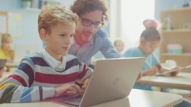 İlköğretim Okulu Bilgisayar Bilimi Sınıfı: Akıllı Çocuk Laptop Bilgisayar Kullanıyor, Arkadaş Canlısı Öğretmen Ders Açıklayarak Ona Yardım Ediyor. Çocuklar BTMM 'de Modern Eğitim Alırken, Oynarken ve Öğrenirken