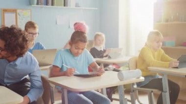 İlköğretim Okulu Bilgisayar Bilimi Sınıfı: Akıllı Kız Dijital Tablet Bilgisayar kullanıyor, Sınıf arkadaşları dizüstü bilgisayarlarla çalışıyor, Sınıfta Arkadaş Canlısı Öğretmen Çocuklara Yardım Ediyor. Çocuklar Modern Eğitime Gidiyor