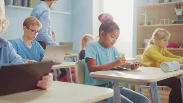 Escola Primária de Ciência da Computação Classe: Menina bonito usa computador tablet digital, seus colegas de classe trabalhar com laptops também. Crianças obtendo educação moderna em STEM, brincando e aprendendo — Vídeo de Stock