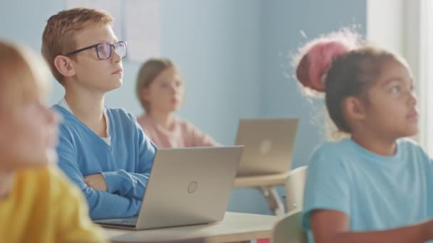 Elementary School Computer Science Class: Smart Boy verwendet Laptop-Computer, seine Klassenkameraden arbeiten mit Laptops, alle hören aufmerksam auf den Lehrer. Kinder bekommen moderne Bildung — Stockvideo