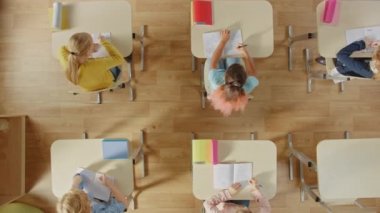 İlköğretim Okulu Sınıfı: Okul masasında oturan çocuklar Egzersiz Defterleri ödevleri üzerinde çalışıyorlar. Üst Görünüm Kamerasını Büyüt.