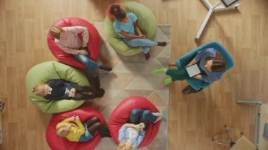 İlköğretim Okulu Yaratıcılık Sınıfı: Öğretmen onlara Dersi Açıklarken ve Dijital Tablet Bilgisayar Kullanırken Çocuklar Fasulye poşetlerinin üzerinde oturuyor. Üst Görünüm Kamerasını Büyüt