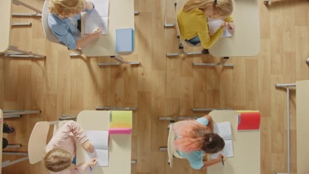 Aula de la escuela primaria brillante: Niños sentados en su escritorio escolar trabajando en asignaciones en cuadernos de ejercicios. Zoom de vista superior de la cámara de tiro . — Vídeo de stock