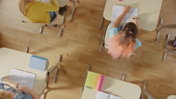 Grundschulklassenzimmer: Kinder, die an ihrem Schultisch sitzen und Aufgaben in Aufgabenheften bearbeiten. Vergrößern Kameraaufnahme von oben. — Stockvideo