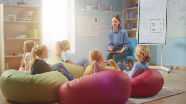 Grundskola Kreativitet klass: Barn sitter på bönpåsar medan Kind Lärare förklarar lektion när du använder digitala surfplatta dator. Smarta barn lär sig i vänlig modern miljö — Stockvideo