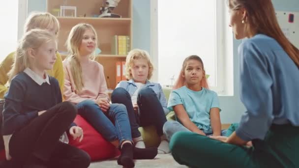 Classe di creatività della scuola elementare: i bambini seduti sul tappeto mentre l'insegnante spiega la lezione e fa domande, ogni bambino alza la mano con la risposta. Imparare in un ambiente moderno — Video Stock