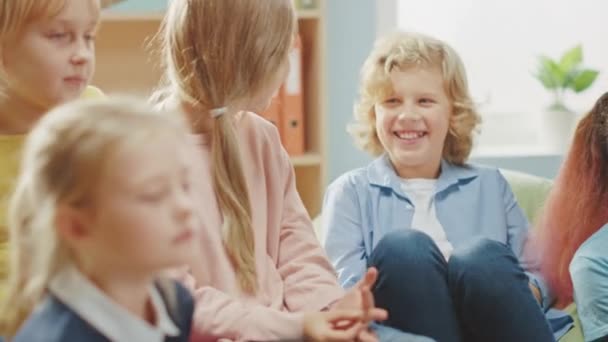 小学校の創造性クラス:子供たちはカーペットの上で一緒に座って先生と話を聞いて楽しい時間を過ごしています。教室での可愛い女の子と男の子の笑顔 — ストック動画