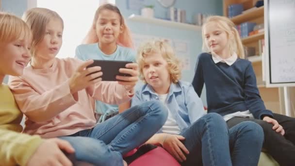 Kinder surfen im Internet und spielen Online-Videospiele auf dem Handy, sehen Videos. Vielfältige Gruppe von niedlichen kleinen Kindern, die gemeinsam auf den Bohnensäcken sitzen, nutzen Smartphone und unterhalten sich, haben Spaß. — Stockvideo