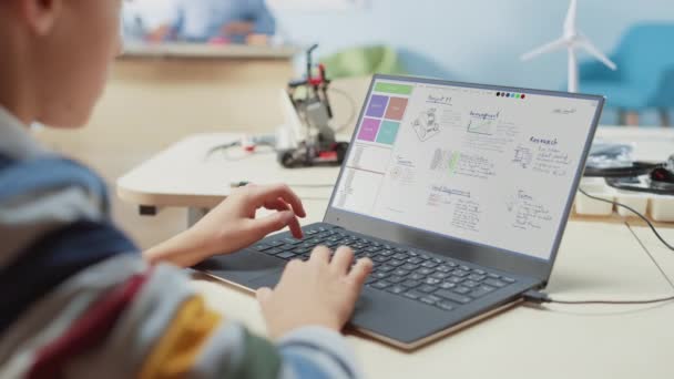 Класс информатики начальной школы: над плечом ребенка, использующего ноутбук для проектирования и программирования робота для класса робототехники — стоковое видео