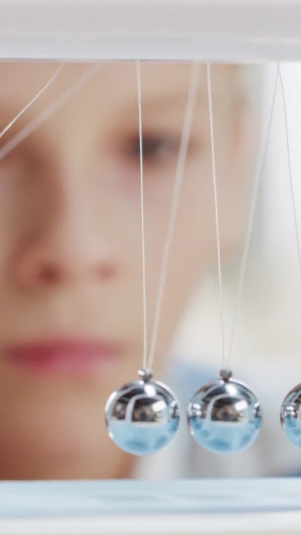 Close-up Portret van een nieuwsgierige jongen kijkend naar Newton 's Cradle. Kind leren over natuurkunde. Videobeelden met verticale schermoriëntatie 9: 16 — Stockvideo