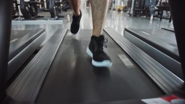 Athletic Muscular Man Correndo em uma esteira, perna e Cardio Day. Forte Homem Treinamento no Ginásio Moderno. Sports People Treino em Fitness Club. Vista frontal de tiro no solo baixo com foco em pernas — Vídeo de Stock