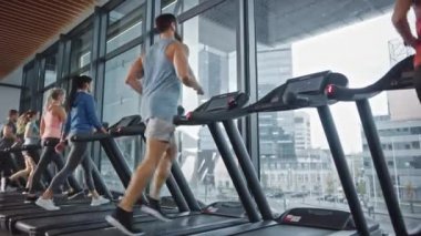 Kaslı Erkek Sporcu, Kablosuz Kulaklıkla Koşu bandında Koşarken Podcast ya da Spor Müzik Listesi dinliyor. Arka planda Güzel Kadın Eğitimi. Yan Görünüm Yükseltiliyor