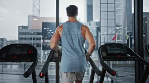 在跑步机上跑步的运动健将,腿和心肺日.具有窗口城市景观的现代健身俱乐部中的强壮男子训练。后视镜慢镜头 — 图库视频影像