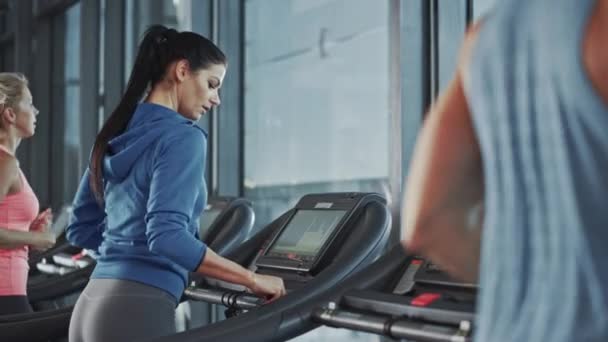 Fit atletická žena běží na běžeckém pásu, dělá její fitness cvičení. Svalové ženy a muži Aktivně trénují v moderní tělocvičně. Cvičení sportovců ve Fitness Clubu. Pomalý pohyb pohledu z boku — Stock video