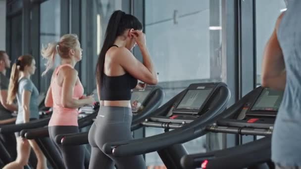 Beautiful Athletic Sports Woman Puts on Wireless Headphones, Turns on Podcast / Music Playlist with Smartphone and Starts Running on a Treadmill in the Gym. Slow Motion Side View — Stock Video