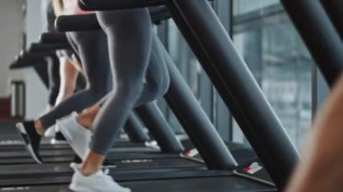 Kablosuz kulaklık takan güzel sporcu kadın, koşu bandında koşarken Podcast veya Sport Music Playlist dinliyor. Arka planda Formda Sporcular Spor Salonu Eğitiminde