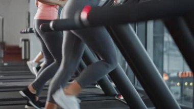 Kablosuz kulaklık takan güzel sporcu kadın, koşu bandında koşarken Podcast veya Sport Music Playlist dinliyor. Arka planda Formda Sporcular Spor Salonu Eğitiminde