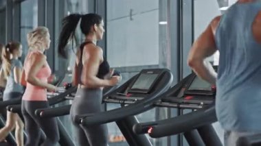 Kablosuz kulaklık takan güzel sporcu kadın, koşu bandında koşarken Podcast veya Sport Music Playlist dinliyor. Spor salonunda formda sporcular antrenmanı. Yan Arka Görünüm