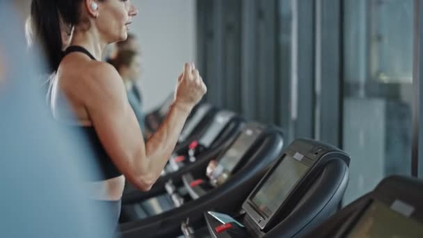 Beautiful Athletic Sports Woman Wearing Wireless Headphones, Listens to a Podcast or Sport Music Playlist while Running on a Treadmill. Fit Athletes Workout in the Gym. Slow Motion Side View — Stock Video