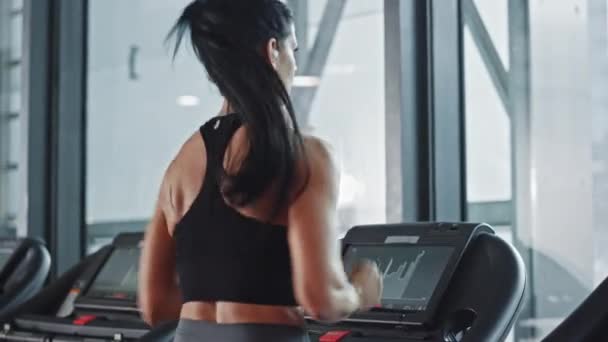 Beautiful Athletic Sports Woman Wearing Wireless Headphones Listens to Podcast or Sport Music Playlist while Running on Treadmill. Energetic Female Athlete Training in Gym Alone. Slow Motion Back View — Stock Video