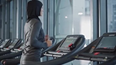 Başörtüsü takan ve koşu bandında koşan Müslüman Atletik Spor Kadını. Sadece Spor Salonu 'nda Enerjik Formda Kadın Sporcu Eğitimi. Kentsel İş Bölgesi Pencere Manzarası. Yan Görünüm Portresi