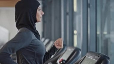 Başörtüsü takan ve koşu bandında koşan Müslüman Atletik Spor Kadını. Sadece Spor Salonu 'nda Enerjik Formda Kadın Sporcu Eğitimi. Kentsel İş Bölgesi Pencere Manzarası. Arka Görünüm Görüntüsü Görüntüsü