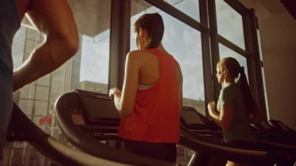 Bela atlética esportiva mulher no ginásio correndo em uma esteira, usa Smartphone. No fundo Fit Athletes Training. Lento movimento baixo ângulo arco tiro. Luz do dia da hora dourada — Vídeo de Stock