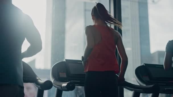 Linda atlética esportiva mulher no ginásio correndo em uma esteira. No fundo Fit Athletes Training. Câmera de movimento lento vista traseira tiro — Vídeo de Stock