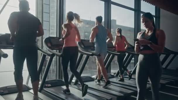 Gyönyörű Athletic Woman használja Smartphone Sétál keresztül Fitness Club Gym. Közösségi média használata, képek közzététele, kommunikáció, e-mail ellenőrzése. A háttérben A futópadokon futó sportemberek — Stock videók
