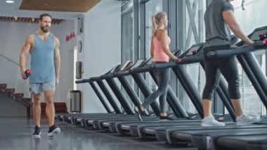 Kas yığını erkek sporcu spor salonuna girer ve koşu antrenmanına koşu bandında ısınma egzersizi olarak başlar. Güçlü ve yakışıklı bir sporcu için Bacak ve Kardiyo Spor Günü. Arka planda Spor İnsanları Eğitiminde