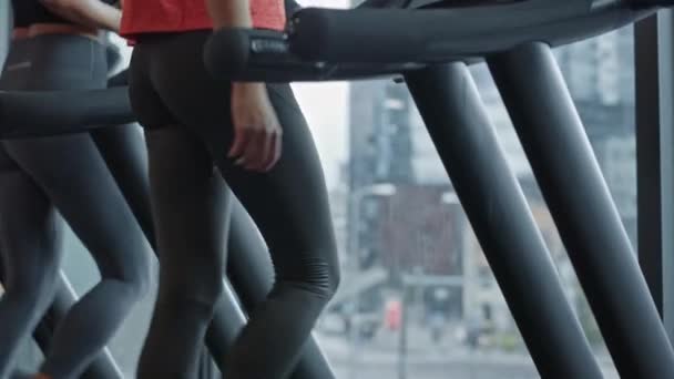 Bella donna sportiva atletica in palestra Correre su un tapis roulant, utilizza lo smartphone. In background si adattano alla formazione degli atleti. Lento movimento elevare vista laterale fotocamera girato — Video Stock