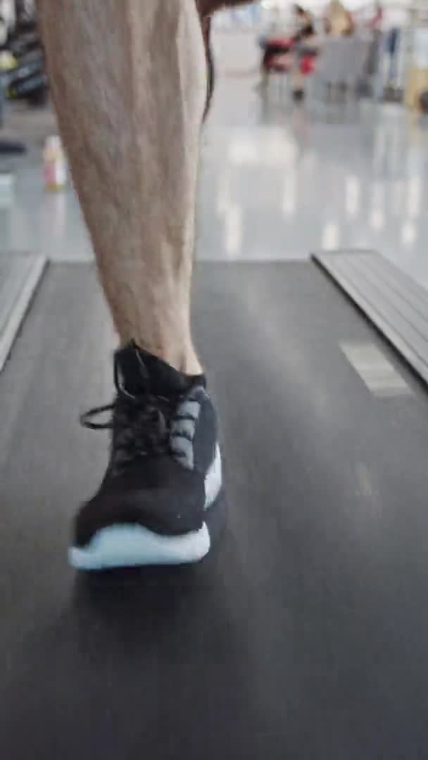 Athletic Muscular Man Running on a Treadmill, Leg and Cardio Day (en inglés). Entrenamiento de hombre fuerte en el gimnasio moderno. Vista frontal de tiro a tierra baja. Concéntrate en Piernas. Vídeo de orientación vertical de la pantalla 9: 16 — Vídeo de stock