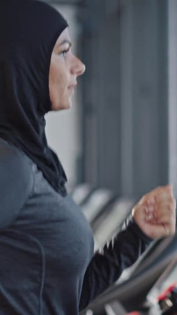 Sportliche muslimische Sportlerin im Hijab, Sportbekleidung auf Laufband. Energetic Fit Athletin Training allein im Fitnessstudio. Seitenansicht Porträt Zeitlupe. Vertikale Bildschirmorientierung Video 9: 16 — Stockvideo