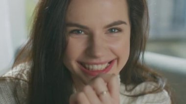 Güzel Genç Esmer 'in portresi Çekici bir şekilde gülümseyerek Kameraya bakıyor, gür saçlarını cilveli bir hareketle fırçalıyor. Beyaz örgü süveter giyen utangaç kız Samimi odada gülüyor