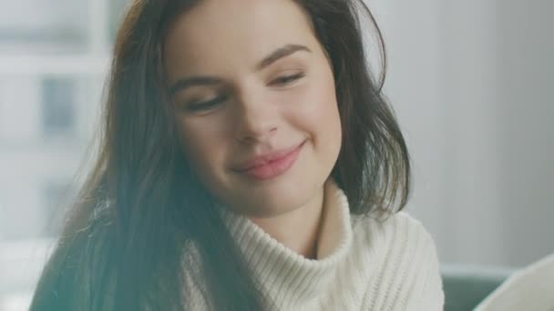 Hermosa mujer joven usando el teléfono inteligente felizmente, mientras está sentado en la silla. Sensual Girl Wearing Knitted Sweater Navega por Internet, Mensajes en las redes sociales, Compartir imagen mientras se relaja en Cozy Apartment — Vídeos de Stock