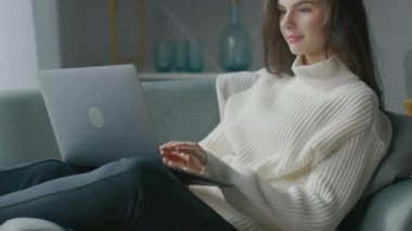 Güzel Genç Kadın, dizüstü bilgisayarda çalışırken sandalyede oturuyor. Süveter giyen Şehvetli Kız Not Defteri 'nde çalışır, çalışır, internette sörf yapar, rahat bir dairede dinlenirken sosyal medyayı kullanır