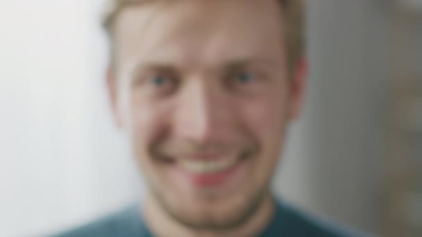 Portrét pohledného blonďatého mladého muže s úsměvem při pohledu na kameru. Šťastný atraktivní chlap s modrýma očima. Fotoaparát se postupně zaměřuje na obličej — Stock video