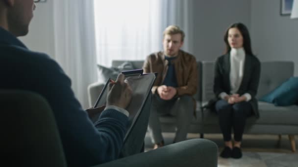 Couple en séance de counseling avec psychothérapeute. Plein feux sur le dossier du thérapeute Prendre des notes et parler : les gens assis sur le canapé de l'analyste, discuter des problèmes psychologiques — Video