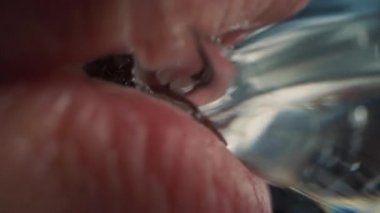 Saydam bir bardaktan içme suyu içen bir insanın aşırı yakın çekim makro çekimi. Taze musluk suyu ağızda akıyor. Kusursuz Beyaz Dişli ve Kırmızı Dudaklı Doğal Ağız.