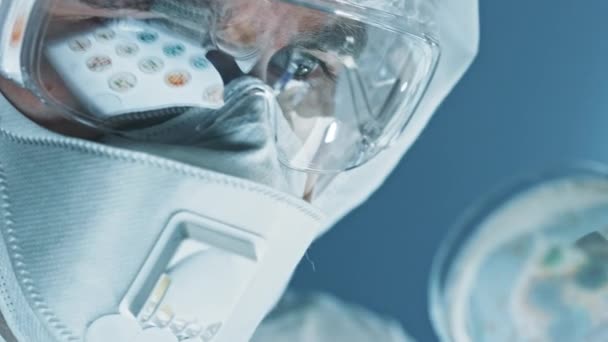 Науковець, який носить Respirator Mask, CGeneral and Safety Glasses looks at Petri Dishes with Bacteria, Tissue and Blood Samples. Лабораторія медичних досліджень Лікування епідемічних захворювань. Збільшений Макро. — стокове відео