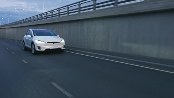 Images parallèles d'un VUS électrique blanc de luxe moderne circulant sur l'autoroute urbaine à l'aube. Voiture alimentée par batterie se déplaçant à travers la route de ville vide. Véhicule futuriste avec phares au xénon . — Video