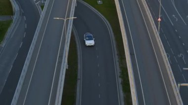 Bulutlu Bir Gün sırasında Şehir Kavşağı 'nda Modern Lüks Beyaz Elektrikli SUV' nin Hava Aracı Görünümü. Pille çalışan araba köprünün altından geçiyor ve otobana giriyor. Panoramik Çatılı Geleceğin Arabası.